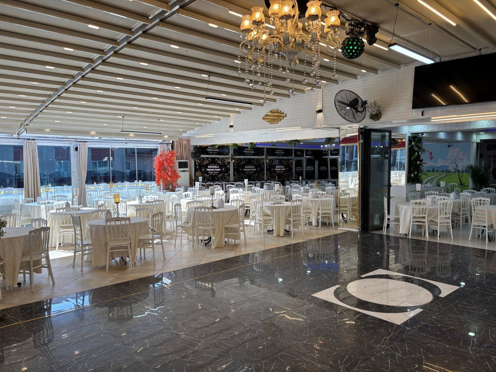 Açılır tavanlı salonda kristal avize, mermer pist ve cam cephe önündeki yuvarlak masalar