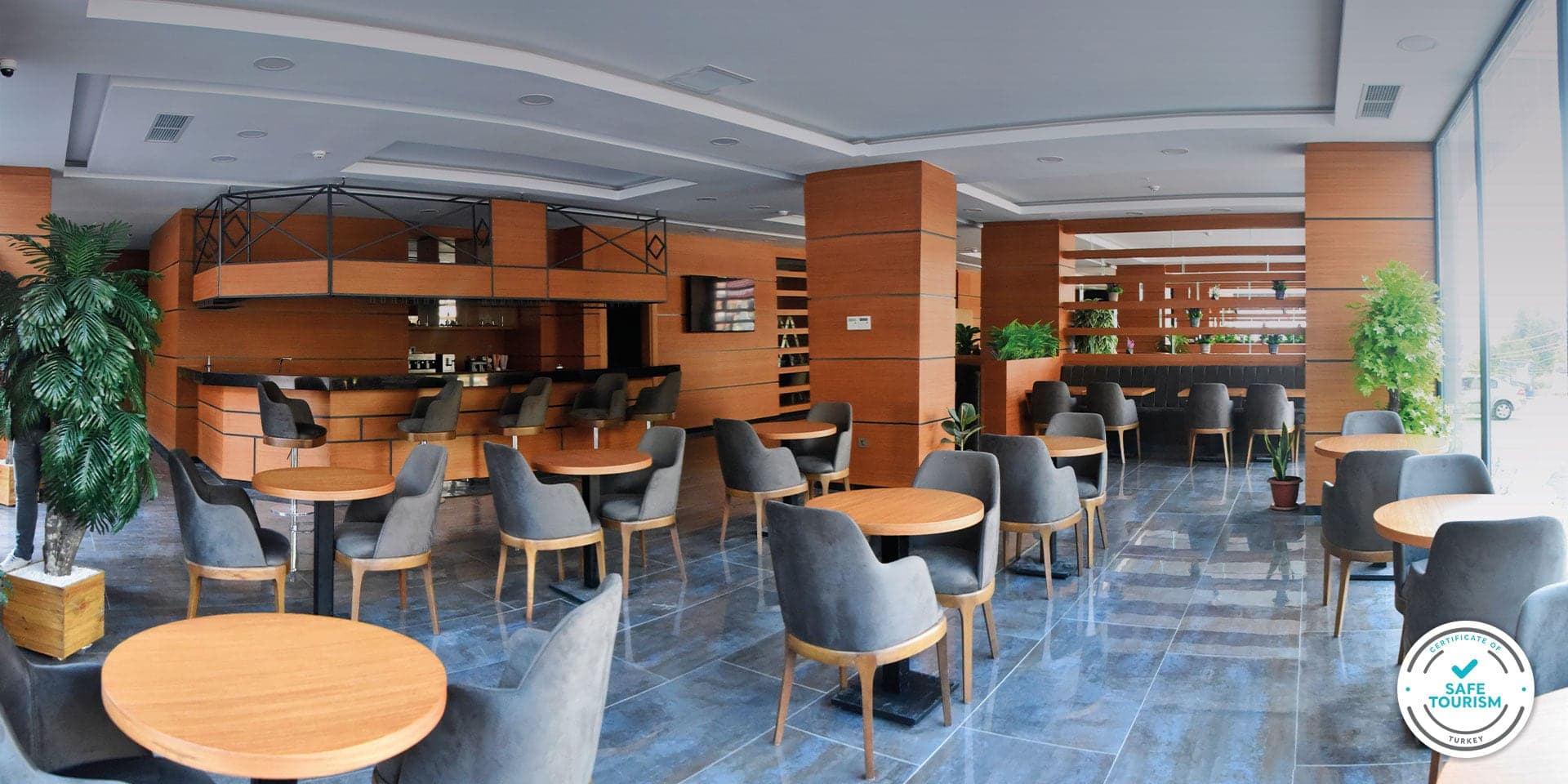 Restoranda ahşap kaplı bar ve yuvarlak masaların çevresinde gri koltuklar