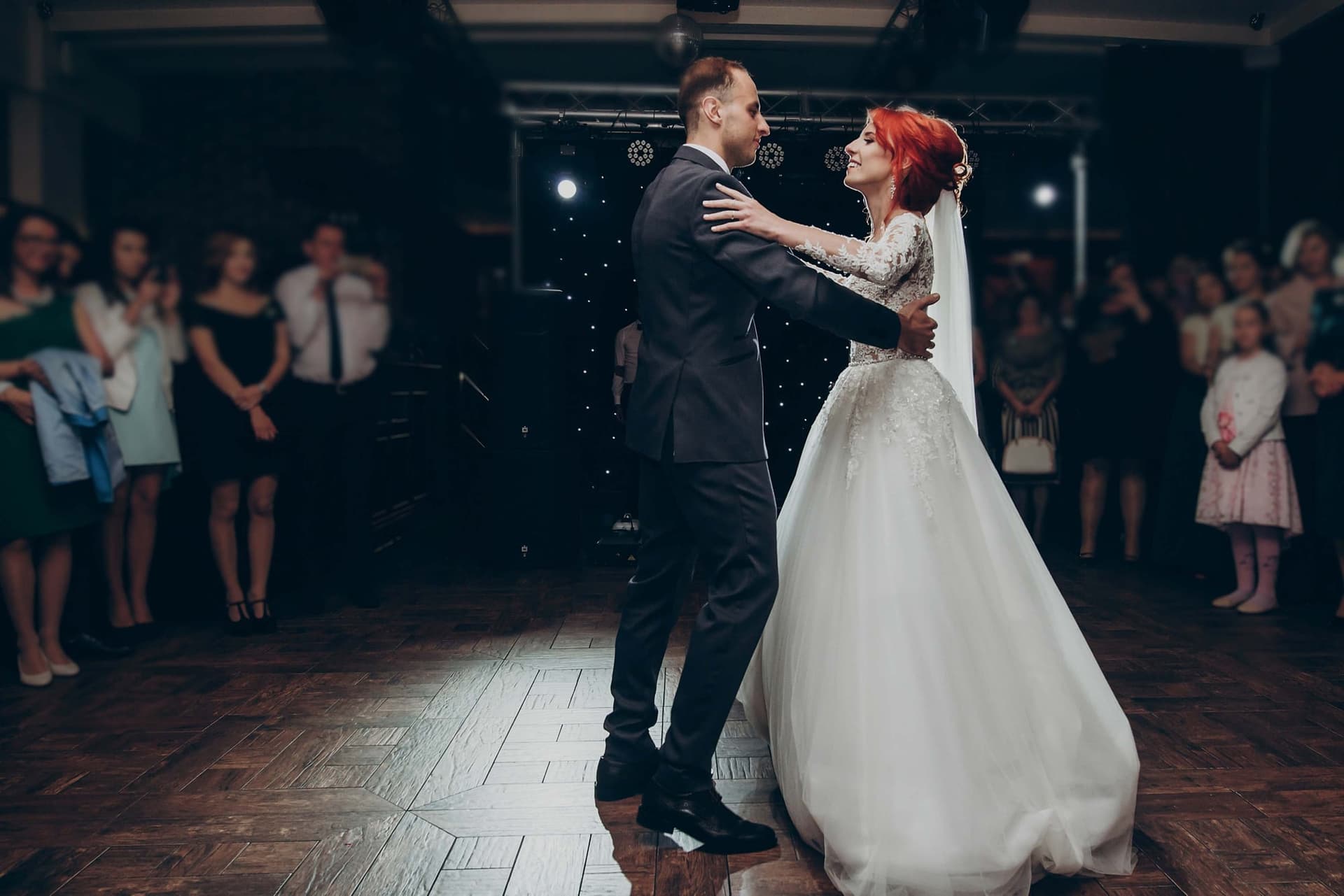 Loş salonda parke zeminde ilk dansını yapan gelin ve damat, çevrede izleyen davetliler