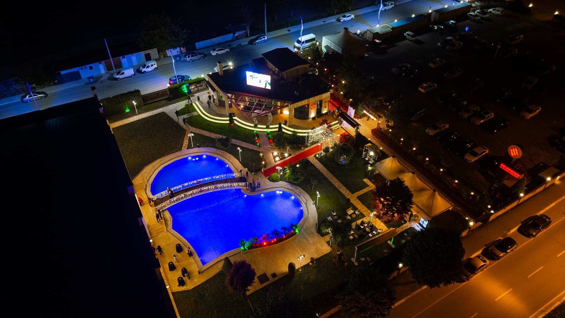 Kalp biçimli ışıklı havuz ve salon binasının gece drone çekimi