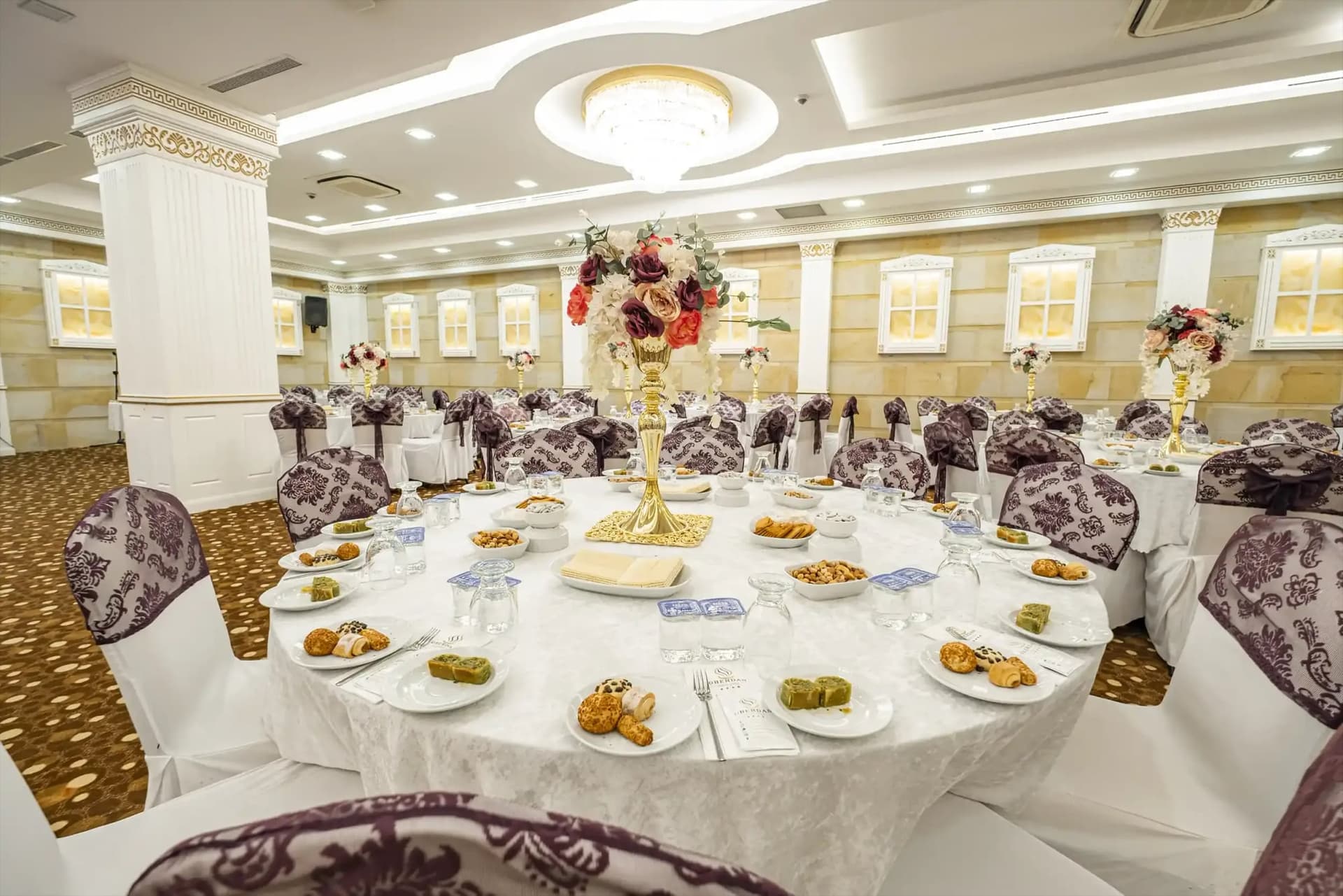 Altın ayaklı çiçek süslü masa, arkada sütunlu salon