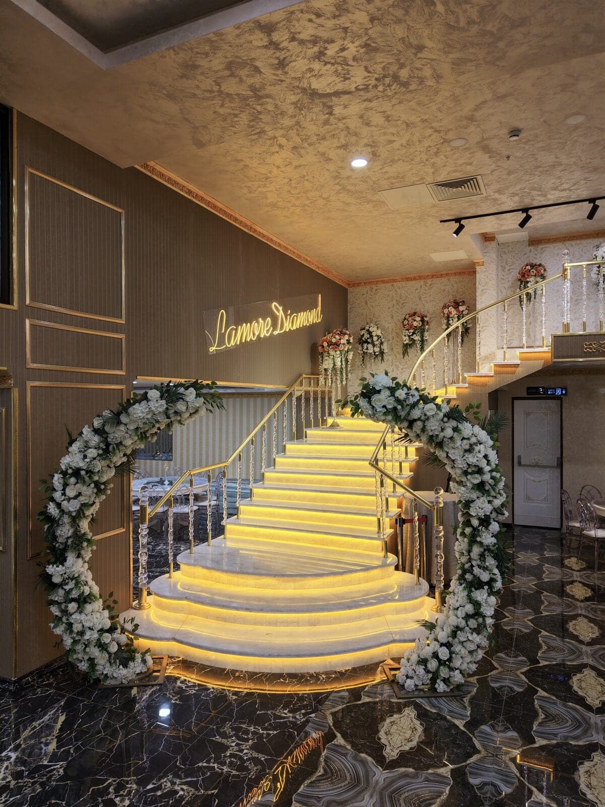 Diamond Salon'da ışıklı merdiven, çiçekli çember süsleme ve duvardaki Lamore Diamond yazısı