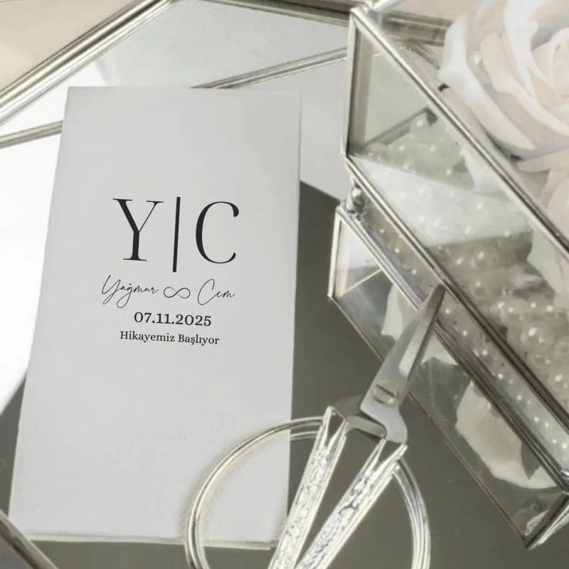 Monogram ve tarih baskılı beyaz düğün peçetesi, cam kutu ve makas yanında