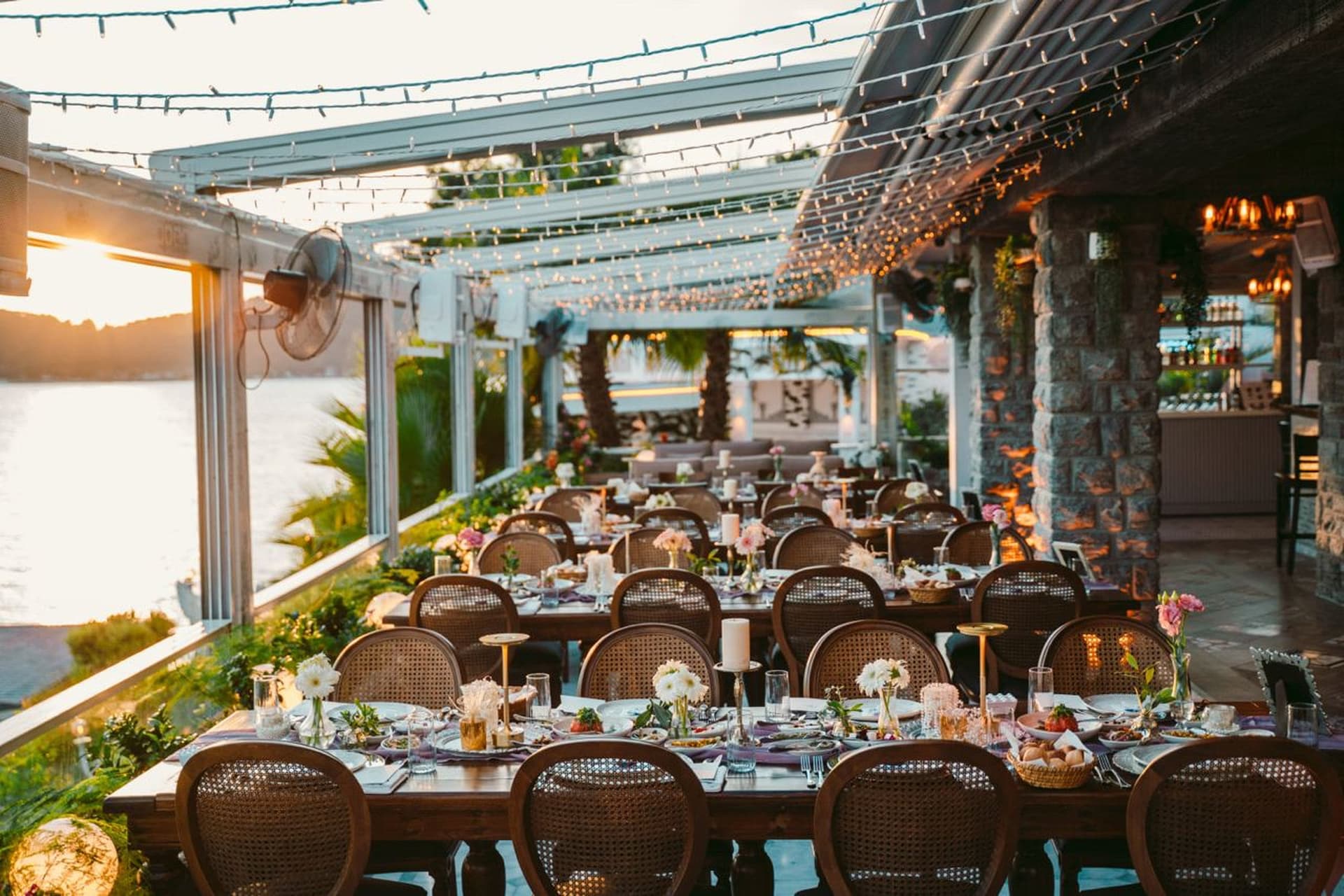 Gün batımında çiçeklerle süslenmiş yemek masaları ve taş kolonlu teras
