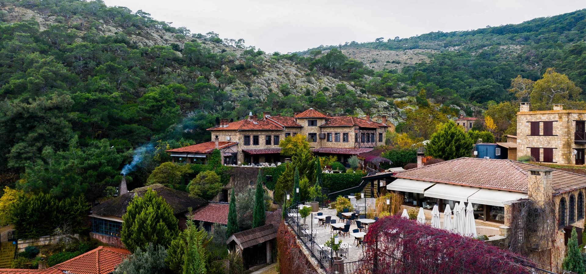 Dağ eteğindeki otel binaları ve beyaz şemsiyeli teras, yukarıdan