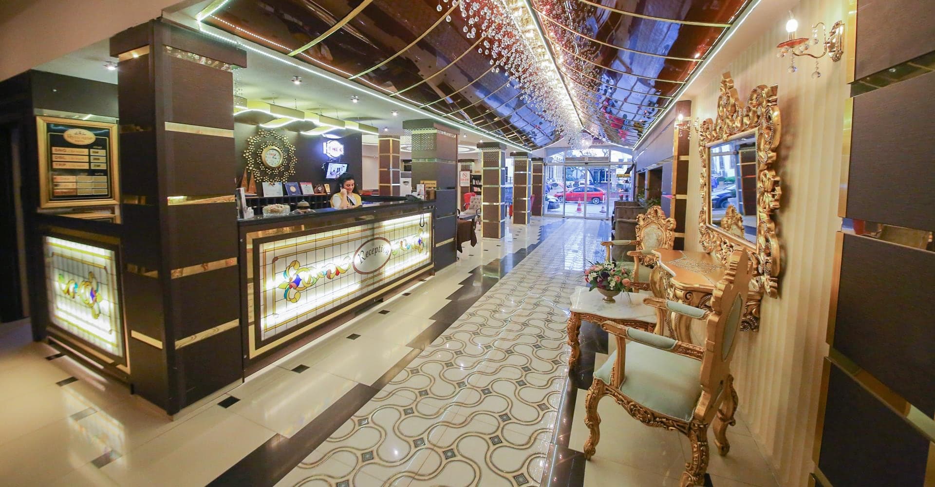 Resepsiyon bankosu, yaldızlı ayna ve ışıklı tavanla otel giriş koridoru