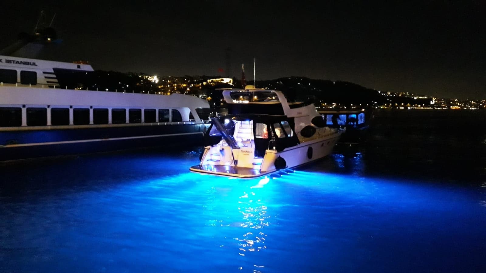 Gece rıhtımda su altı mavi ışıklarıyla aydınlatılmış yat