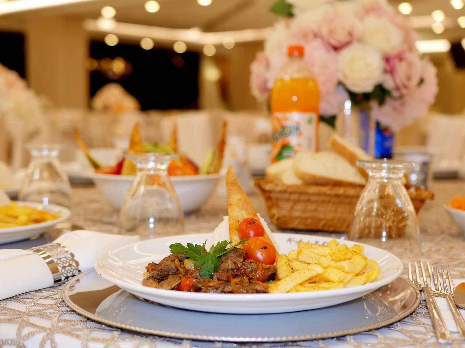 Çiçek süslemeli düğün masasında etli yemek tabağı, ekmek sepeti ve bardaklar