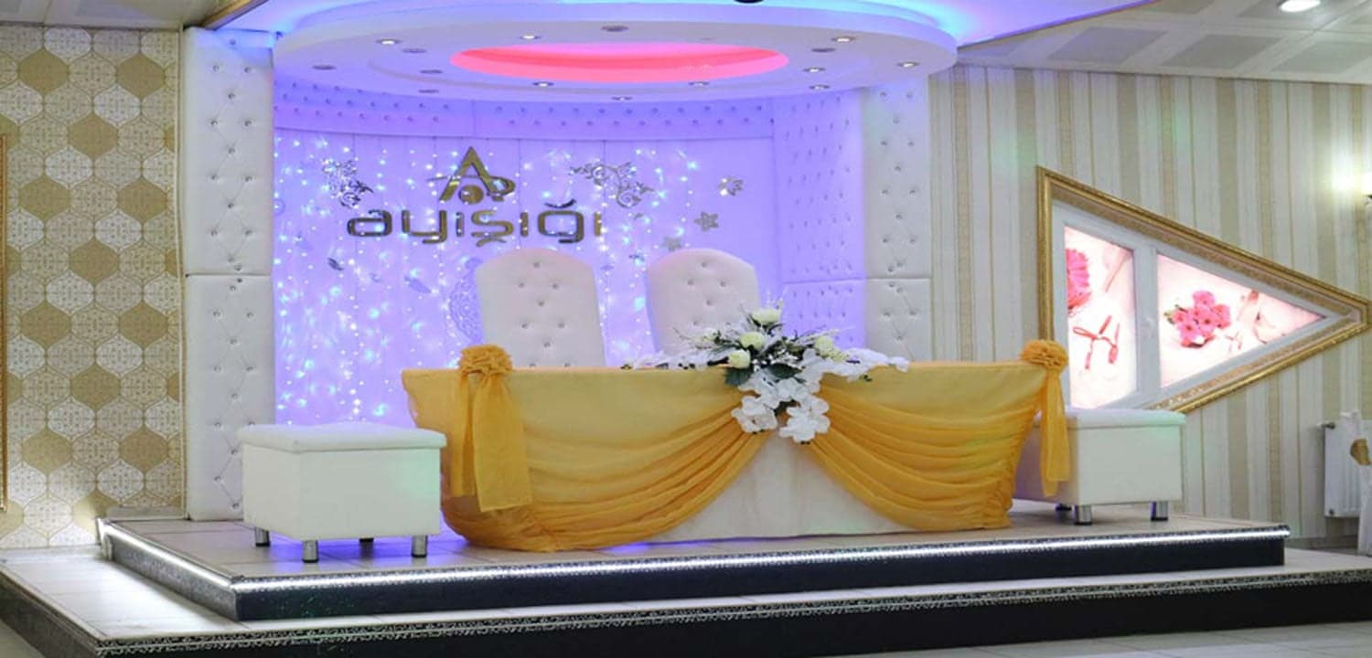 Mor ışıklı sahnede sarı tül süslü gelin damat masası ve beyaz koltuklar