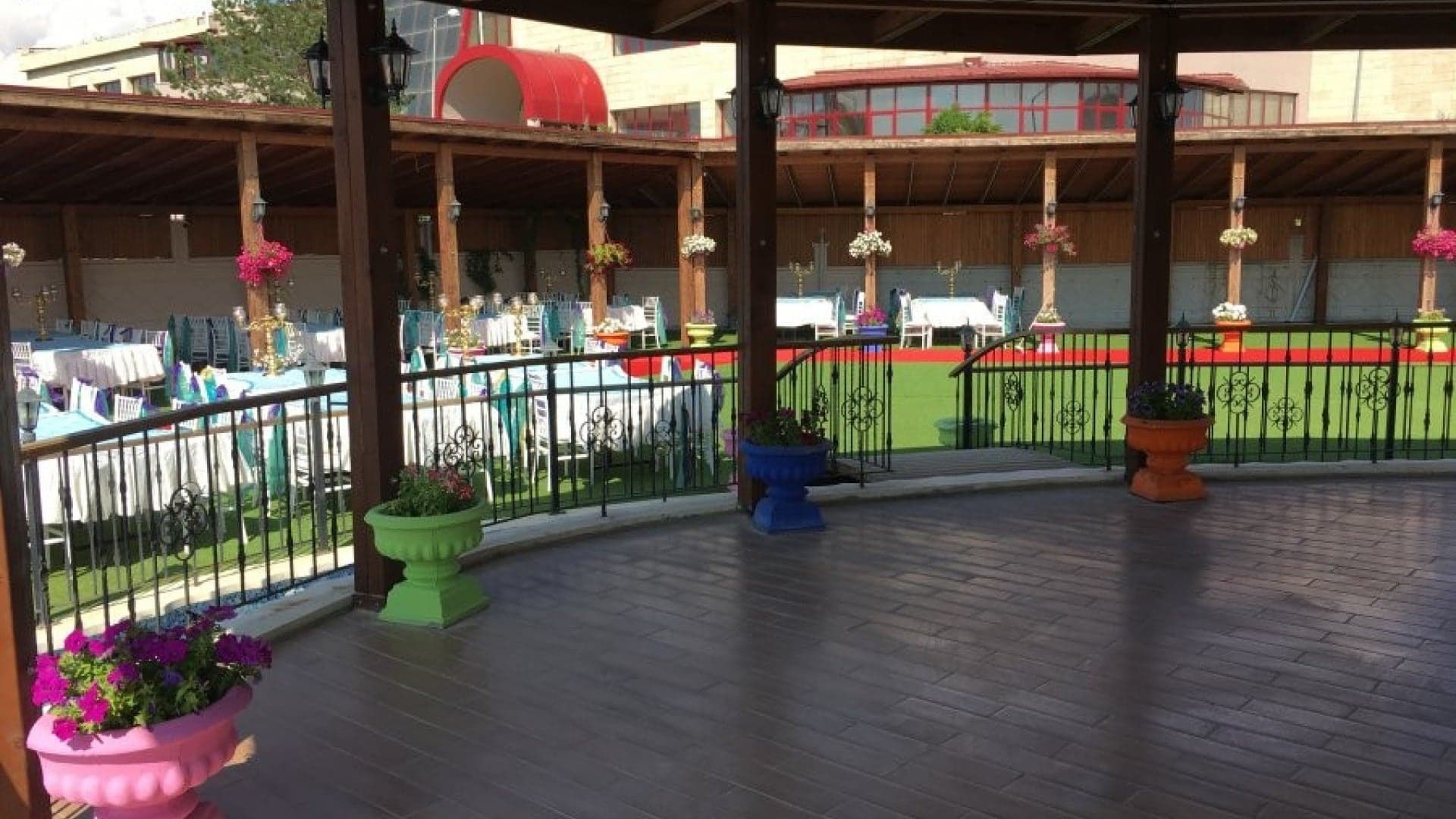 Verandanın ahşap zeminli kavisli köşesi, saksı çiçekleri ve avluya bakan korkuluk