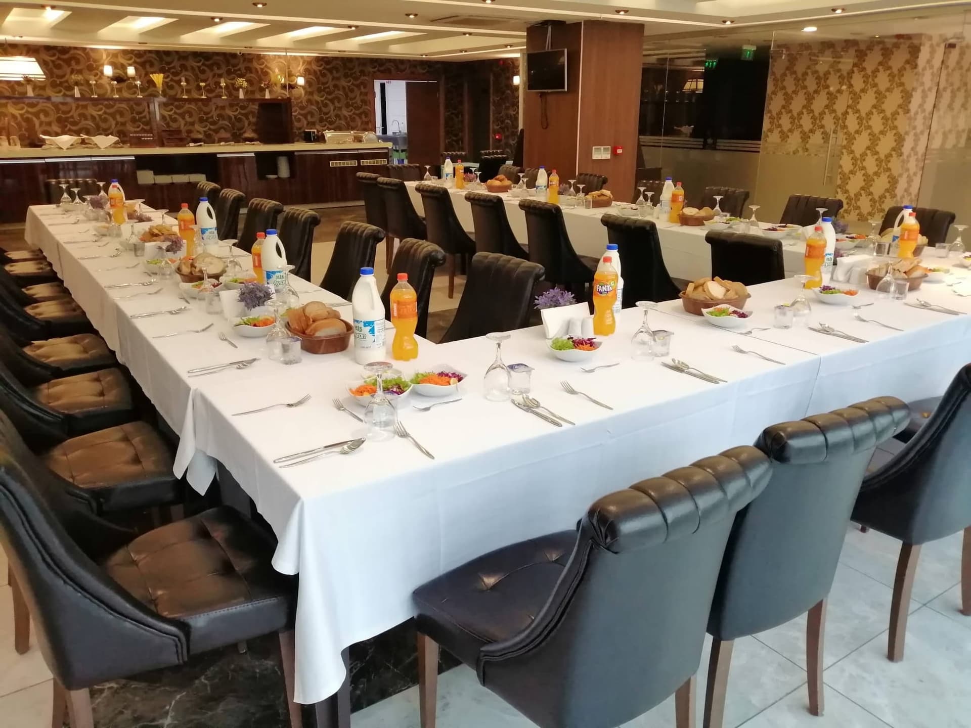 Siyah deri sandalyeli uzun masada kurulmuş yemek düzeni