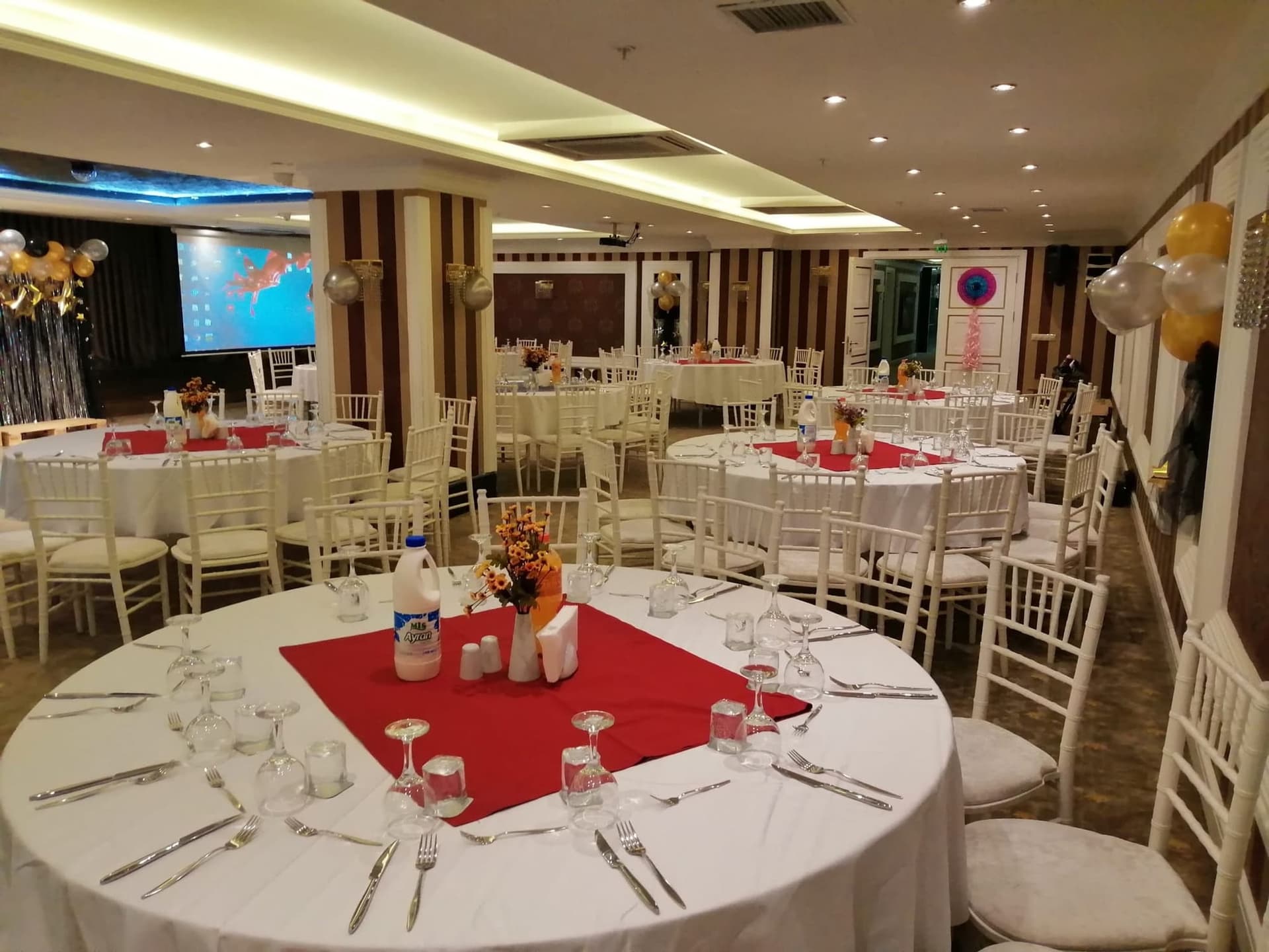 Royal Hotel İnegöl salonunda kırmızı örtülü yuvarlak masalar ve balon süsleri