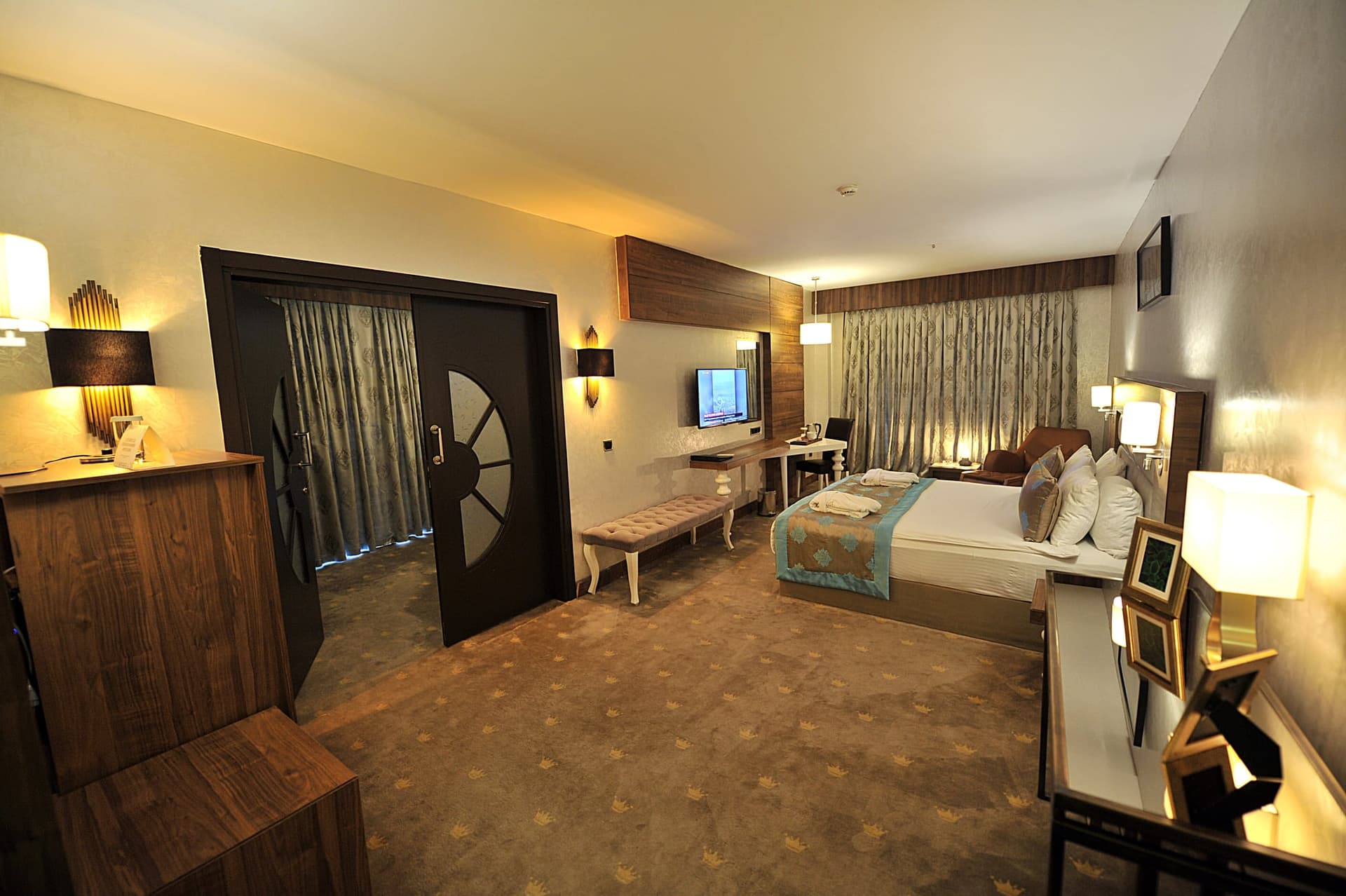 Geniş otel odasında çift kişilik yatak, oturma bankı ve ahşap çift kanatlı kapı