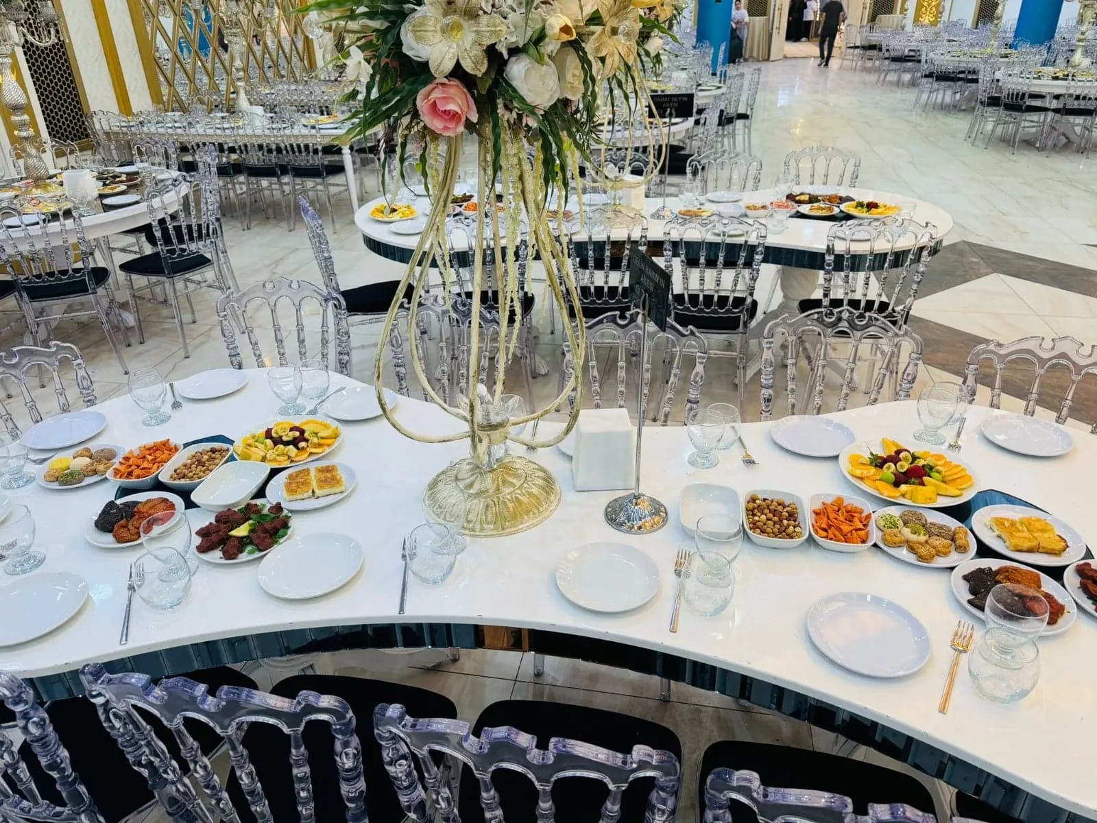 Yuvarlak masalarda meze tabakları ve uzun ayaklı çiçek aranjmanı