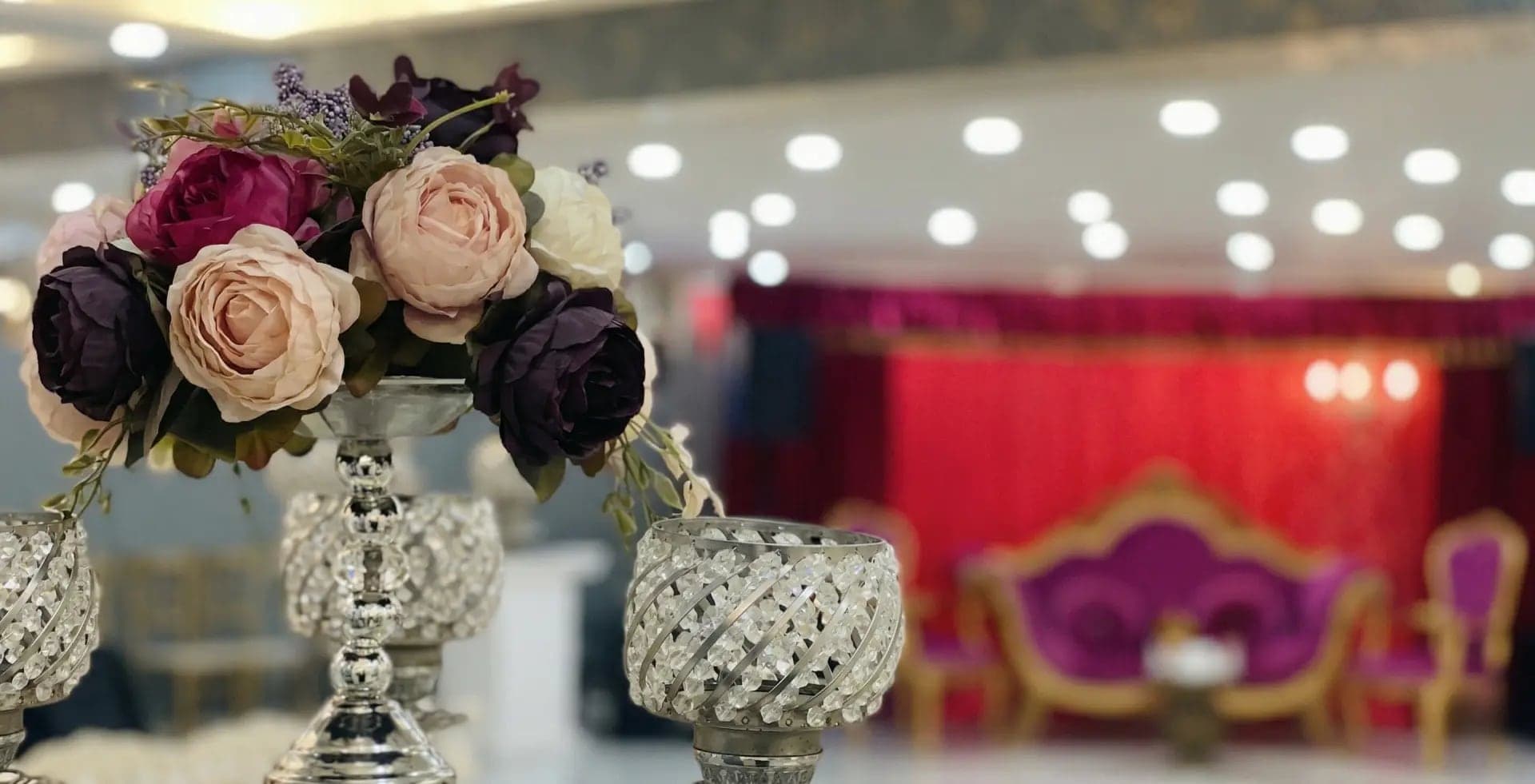 Kristal şamdanlı masa süsü, arkada kırmızı perde önünde mor kadife koltuklar