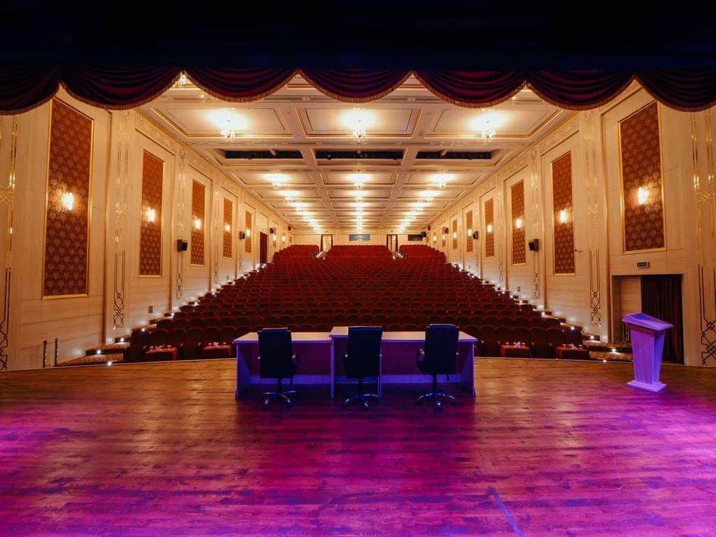 Mor ışıklı sahnesi ve basamaklı koltuk sıralarıyla konferans salonu