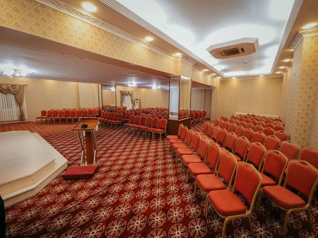 Desenli halı üzerinde kırmızı sandalyelerin dizildiği toplantı salonu