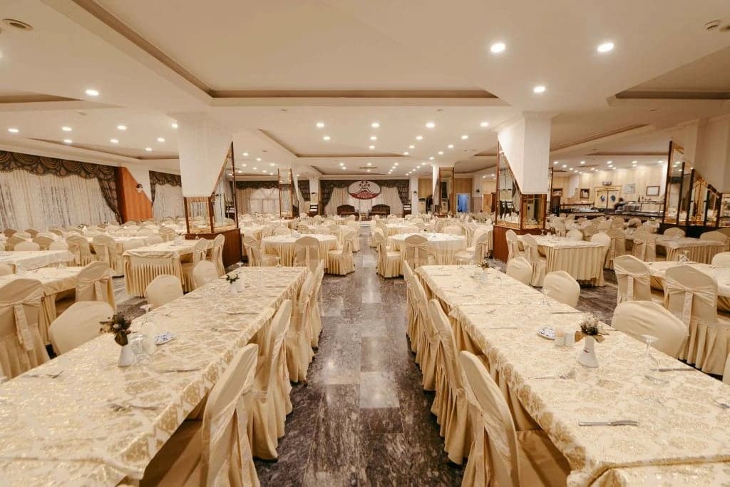 Krem örtülü uzun masalar ve kılıflı sandalyelerle kurulmuş geniş yemek salonu